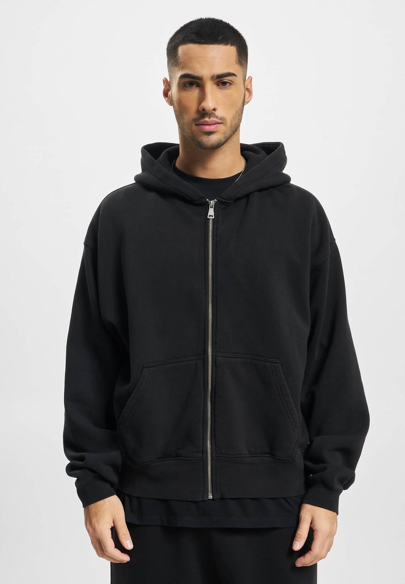 Sort zip-up hættejakke lavet af blødt stof, med en stor hætte, to forlommer og ribbede manchetter. Løs pasform og minimalistisk design.