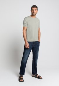 Lichtgrijs T-shirt met korte mouwen en een ronde hals, gecombineerd met donkerblauwe denim jeans en zwarte sandalen, wat een casual look presenteert.