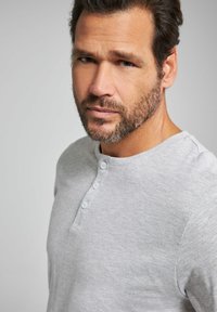 Maglietta henley grigia con scollo rotondo, maniche corte e pattina con tre bottoni. Tessuto morbido e design aderente.