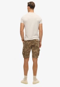  Lichtgrijze T-shirt met korte mouwen, gecombineerd met militaire camouflage cargoshorts met zijzakken, afgewerkt met beige sneakers.