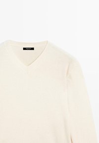 Maglione a V in color crema, realizzato in morbido materiale. Presenta un colletto a coste e un sottile dettaglio di cucitura. Design semplice e classico.