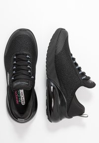 Czarne buty sportowe z siateczkową cholewką, teksturowanym wzorem i gumową podeszwą. Cechy to sznurowadła z jasnoszarymi akcentami oraz błyszczący obcas.