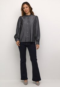 Lesklá tmavě šedá blůza s vysokým ruffled límcem, dlouhými nafouklými rukávy a kulatými knoflíky. V kombinaci s tmavými zvonovými džíny a světlými botami.
