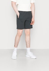 Tmavě šedé, texturované šortky s elastickým pasem, bočními kapsami a délkou do poloviny stehna, v kombinaci s bílými teniskami a ponožkami.