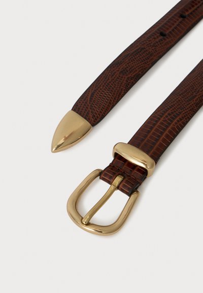 Ceinture en cuir marron texturé avec embout doré pointu et boucle dorée arrondie sur fond blanc.
