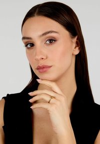 Anello d'oro con un design liscio e arrotondato, indossato sulla mano di un modello, con unghie naturali e trucco sobrio, su uno sfondo neutro.
