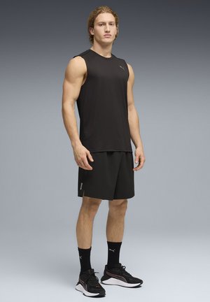 Canotta sportiva nera senza maniche con scollo rotondo, abbinata a pantaloncini neri e scarpe da ginnastica nere. Presenta una leggera lucentezza e dettagli con logo.