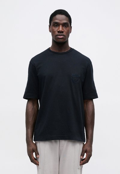 Svart bomullst-skjorte med rund hals og korte ermer. Har en teksturert lomme på venstre bryst. Standard passform og glatt tekstur.