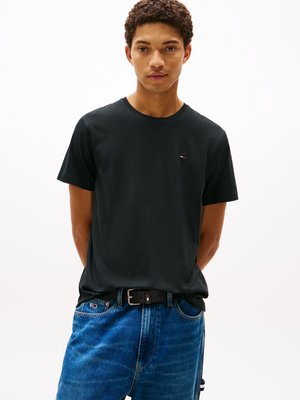 Zwarte katoenen t-shirt met een ronde hals en korte mouwen, voorzien van een klein logo op de borst. Gecombineerd met blauwe denim jeans en een zwarte riem.