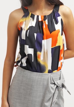 Mujer con top sin mangas con patrones abstractos en negro, blanco, naranja, amarillo y morado combinado con falda gris de talle alto con nudo lateral.