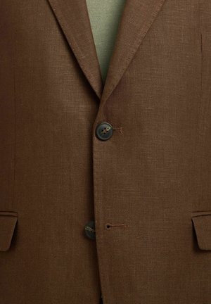 Blazer marron texturé avec revers cranté, deux boutons foncés fermés et poches à rabat de chaque côté sur un vêtement vert.