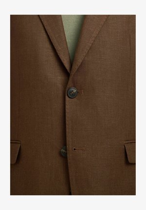 Blazer marron texturé avec revers cranté, deux boutons foncés fermés et poches à rabat de chaque côté sur un vêtement vert.