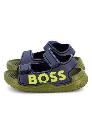 Marineblauwe sandalen met groene rubberen zolen, voorzien van twee verstelbare klittenbandbandjes en een opvallend geel "BOSS"-logo aan de zijkant.