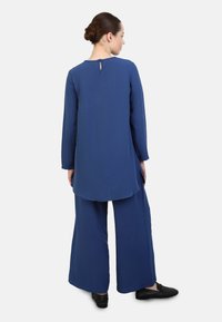 Blue two-piece outfit with a long tunic featuring a round neck and keyhole back, paired with wide-leg pants, made of soft fabric.
