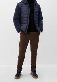 Giacca puffer blu navy con maniche in pile testurizzato, dolcevita nero, joggers marroni e sneaker nere con suola beige.