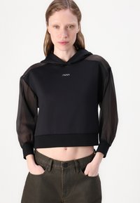 Μαύρο κοντό φούτερ με λείο σώμα και διάφανα, φουσκωτά μανίκια. Περιλαμβάνει το λογότυπο DKNY σε ασημί χρώμα στο κέντρο εμπρός.