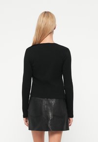 Μαύρο μακρυμάνικο ριμπ τοπ με στρογγυλή λαιμόκοψη, σε συνδυασμό με μαύρη μίνι δερμάτινη φούστα ψηλής μέσης με δύο πίσω τσέπες.