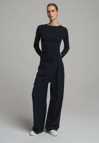 Granatowa bluzka z długim rękawem połączona z szerokimi spodniami w granatowe paski i białymi trampkami. Teksturowana tkanina, luźny krój, minimalne dodatki.