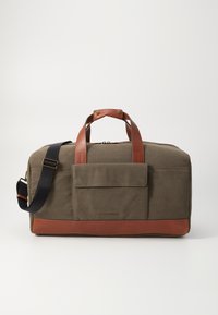 Duffle bag made of olive green fabric with brown leather accents and a black adjustable strap. Features a front pocket and zip closure.