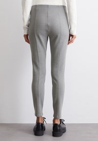 Leggings aderenti grigi realizzati in un tessuto elasticizzato, con una consistenza liscia e cuciture visibili; abbinati a scarpe nere con lacci.