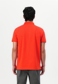 Rød polo-shirt med klassisk krave, korte ærmer, sideåbninger og en glat tekstur, set fra ryggen.