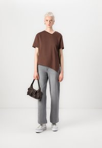 Brun asymmetrisk v-hals t-skjorte, grå rette jeans, hvite platå sneakers og en liten mørk håndveske. Enkelt, uformelt antrekk.
