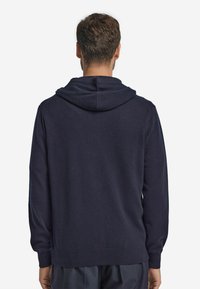 Marinblå hoodie av mjukt material med snörning i huvan, långa ärmar och ribbade muddar och fåll. Enkelt design utan synliga mönster.