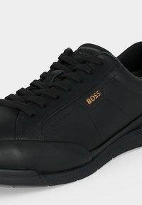 Baskets en cuir noir avec lacets noirs, semelle texturée et logo BOSS doré sur la partie latérale.