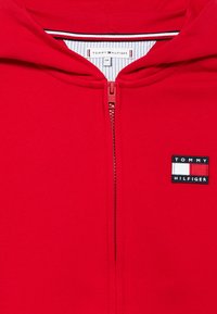 Ερυθρό φούτερ με φερμουάρ από βαμβακερό μείγμα. Διαθέτει μπαλώμα λογοτύπου με μπλε, λευκές και κόκκινες λεπτομέρειες. Σχεδίαση με κουκούλα και ριμπ λεπτομέρειες.