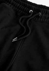 Schwarze Trainingshose mit strukturiertem Finish, ausgestattet mit einem elastischen Bund, verstellbarem schwarzen Kordelzug und glänzenden silbernen Endstücken.