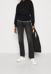 Černá mikina s logem, šedé džíny, bílé tenisky a černá plátěná taška. Uvolněný střih a pohodlný design s minimální texturou.