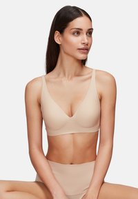 Sujetador bralette sin costuras en tono nude con diseño de escote en V y tirantes finos. Textura suave, estilo minimalista, combinado con una parte inferior de talle alto a juego.