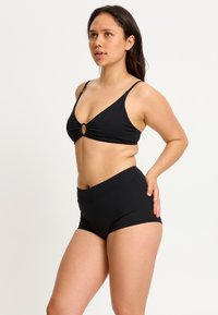 Bikini noir avec un haut triangle et un détail de nœud sur le devant, accompagné de shorts taille haute. Texture de tissu lisse.