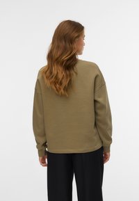 Olijfgroen oversized sweatshirt met ribgebreide manchetten, relaxte pasvorm, ronde hals en zachte textuur. Gemaakt in combinatie met zwarte broeken.