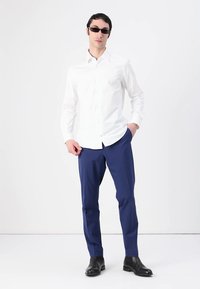 Bílá košile na knoflíky, námořnické kalhoty, černé boty a sluneční brýle. Hladká látka, upravený střih a minimalistický design.