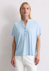 Lichtblauw T-shirt met korte mouwen en een henley halsontwerp, voorzien van drie knopen en een ontspannen pasvorm. Gemaakt van zachte, lichte stof.