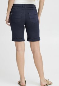Pantalones cortos de mezclilla azul marino con dobladillos enrollados, que cuentan con bolsillos traseros y detalles de costura sutiles, hechos de una tela suave y elástica.
