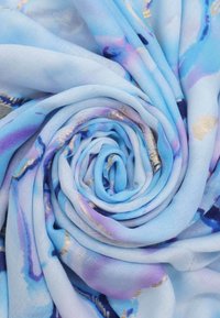 Sciarpa azzurro chiaro con una texture morbida, caratterizzata da motivi in stile acquerello con accenti viola e oro, disposti a forma di spirale.