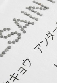 Texturované stříbrné kovové nýty uspořádané na bílém textilním pozadí, s černým tištěným textem v moderním písmovém stylu.