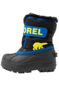Schwarze Schneestiefel mit Gummisohle, blauer Riemen mit "SOREL"-Logo, gelbe Bärengrafik, Kunstfellkragen und strukturierte Oberfläche.