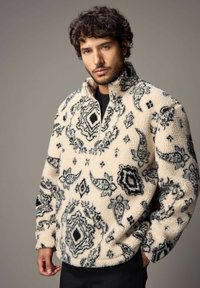 Fleece pullover i creme med sorte paisley-mønstre, halv-zip krave og struktureret overflade. Løs pasform og lange ærmer.