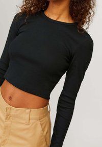 Schwarzes, geripptes Langarm-Crop-Top mit Rundhalsausschnitt, kombiniert mit beigen, hochgeschnittenen Hosen mit seitlichen Taschen und glatter Textur.