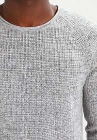 Szary dziergany sweter z teksturowanym wzorem, okrągłym dekoltem i prążkowanymi detalami na ramionach. Miękki, elastyczny materiał.