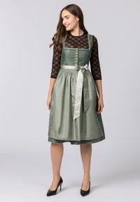 Traditionelles Kleid mit einem grün gemusterten Oberteil, tailliertem Schnitt und einem fließenden Satinsrock. Es verfügt über eine Satinschleife und lange schwarze Spitzeärmel.
