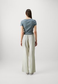 Haut ajusté à manches courtes bleu clair associé à un pantalon large à taille haute gris clair, mettant en valeur la texture du tissu lisse et des lignes épurées.
