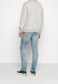 Grå sweatshirt med ribbad mudd, kombinerad med ljusblå distressed jeans och gröna sneakers med vita detaljer. En enkel, avslappnad outfit.