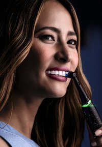 Brosse à dents électrique avec un manche noir arborant un motif étoilé. Tête de brosse bleue et lumière indicatrice verte, gros plan sur un visage souriant.