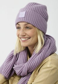 Lila gebreide beanie en sjaal set, met ribbeltextuur en een vierkant logo op de muts. Het garen is zacht en comfortabel.