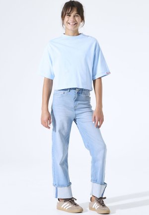 Lichtblauw cropped T-shirt met een ontspannen pasvorm, gecombineerd met lichtblauwe rechte jeans met omslag bij de enkels. Bruine sneakers met witte strepen.