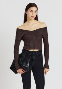 Braunes, geripptes, schulterfreies Crop-Top mit langen Ärmeln, kombiniert mit hoch taillierten schwarzen Jeans. Model hält eine große schwarze Ledertasche.